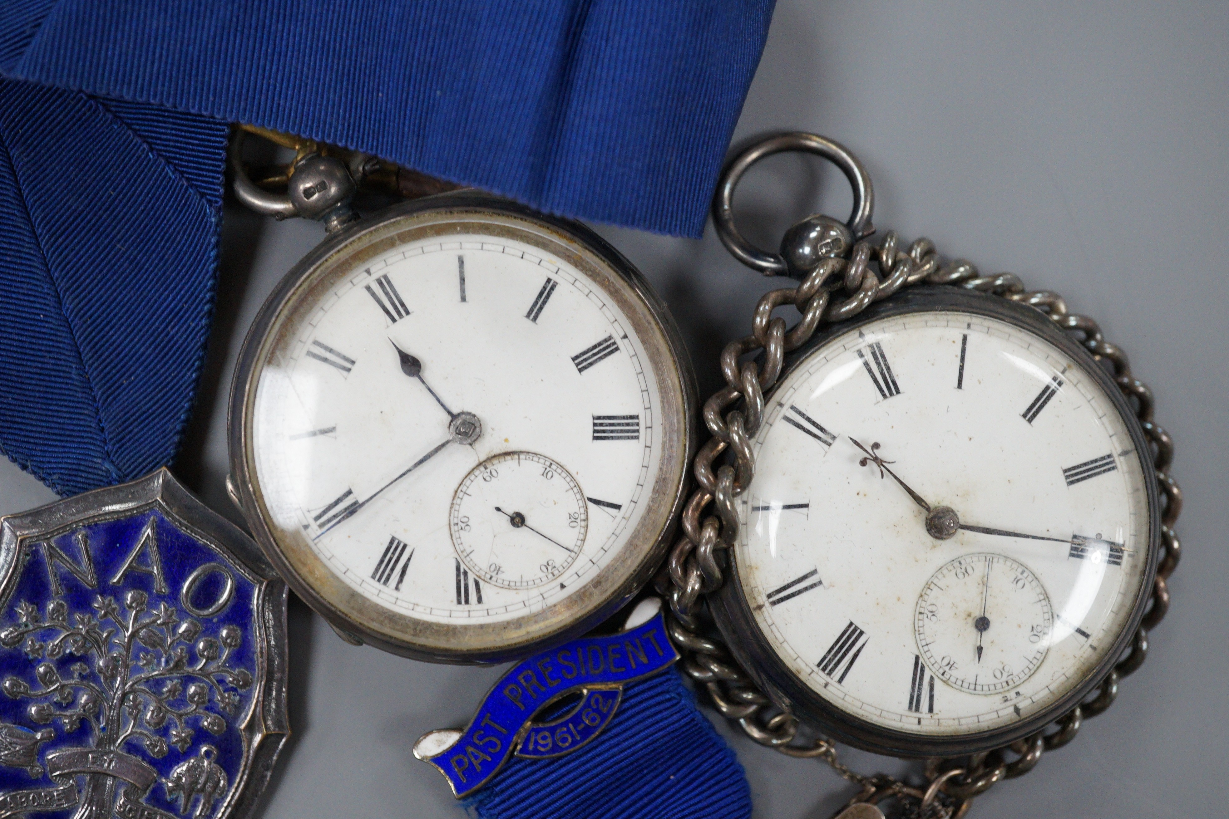 A small collection of silver badges and medals together with two silver pocket watches and a bracelet.